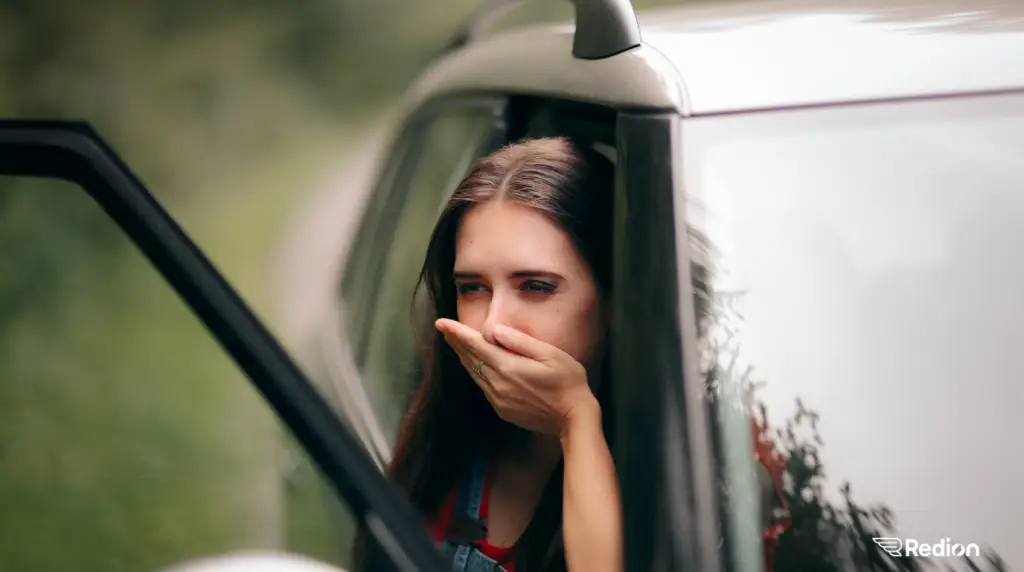 jeune fille à l'avant d'une voiture arrêtée et qui semble malade.