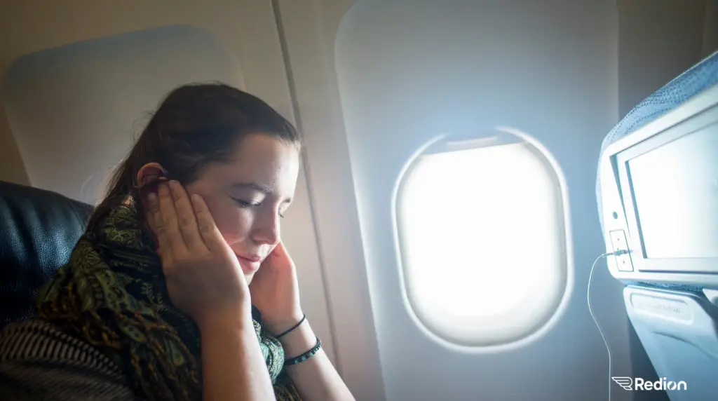 jeune femme dans un avion près du hublot et qui semble avoir mal aux oreilles